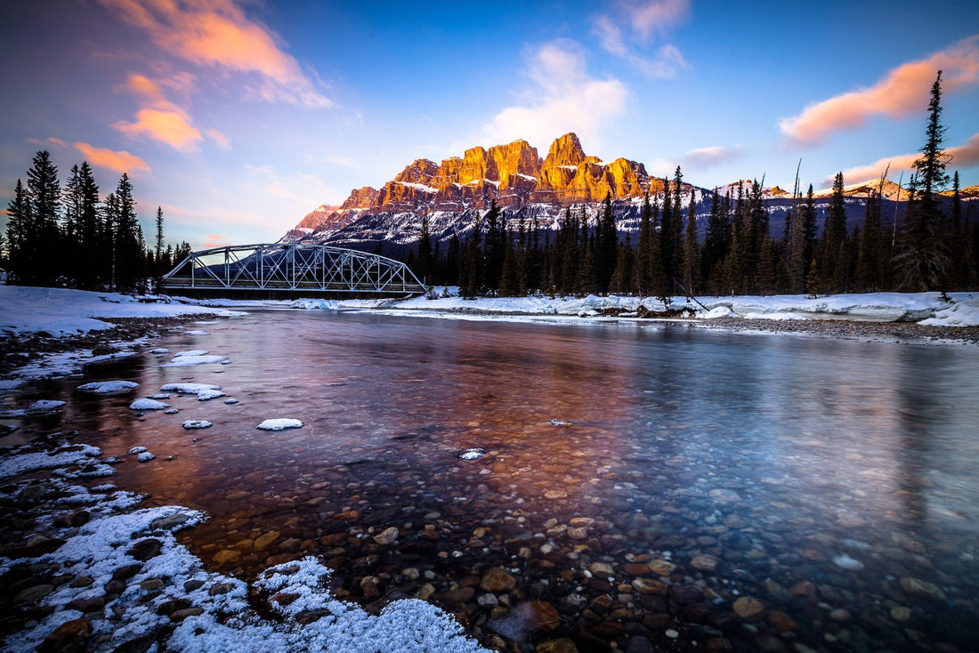 Alpenglow on Castle Mountain above the clear, half-frozen Bow River and a steel bridge, Banff National Park, Canada — fine art photography print by Martin Sojka