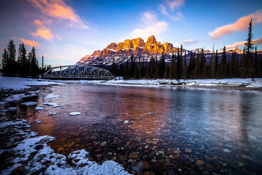 Alpenglow on Castle Mountain above the clear, half-frozen Bow River and a steel bridge, Banff National Park, Canada — fine art photography print by Martin Sojka
